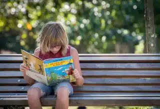 girl in red top sitting on bench while reading